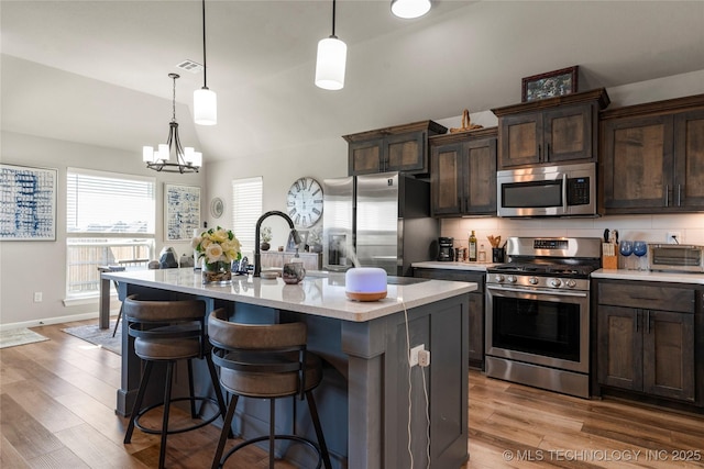 kitchen with dark brown cabinetry, visible vents, appliances with stainless steel finishes, a breakfast bar area, and wood finished floors