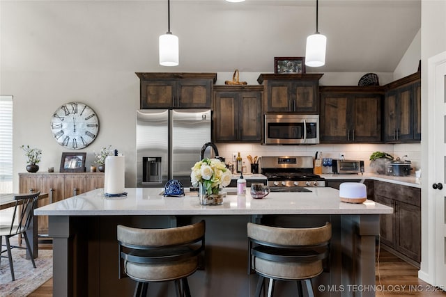 kitchen with appliances with stainless steel finishes, dark brown cabinets, backsplash, and an island with sink