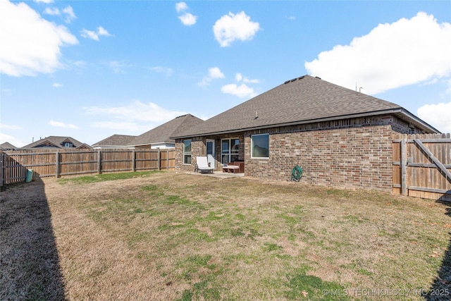 rear view of property featuring brick siding, a yard, and a fenced backyard