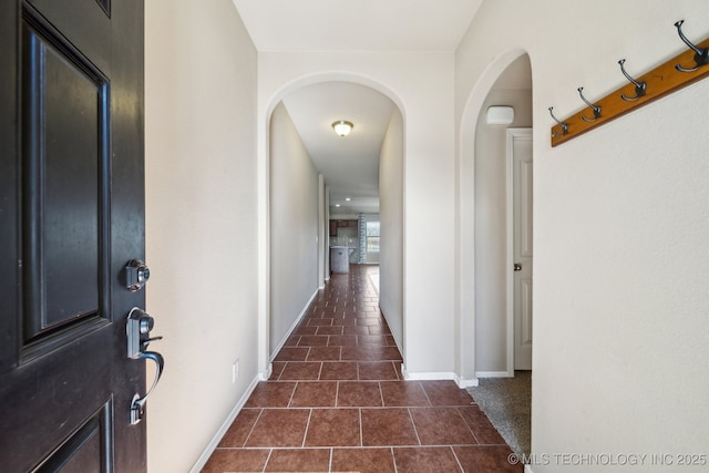 corridor with arched walkways, dark tile patterned floors, and baseboards