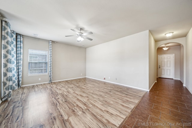 empty room featuring arched walkways, ceiling fan, wood finished floors, and baseboards