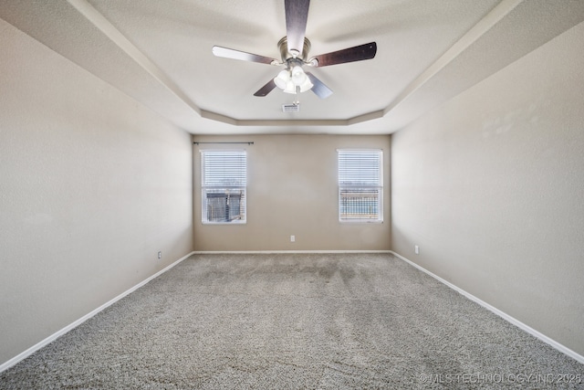 carpeted empty room with ceiling fan, a raised ceiling, visible vents, and baseboards