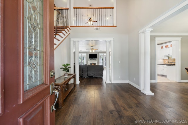 foyer featuring ornate columns, a lit fireplace, visible vents, and dark wood-style flooring