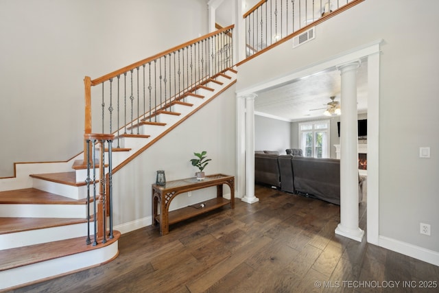 staircase with decorative columns, visible vents, a ceiling fan, wood finished floors, and a lit fireplace