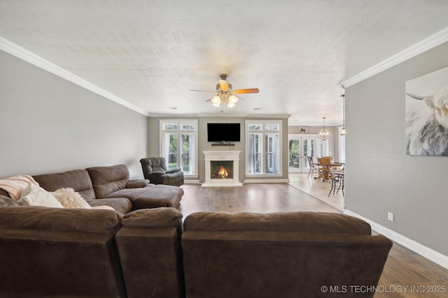 living area with ornamental molding, a textured ceiling, wood finished floors, a lit fireplace, and baseboards