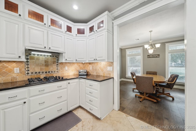 kitchen with white cabinets, dark countertops, ornamental molding, black gas cooktop, and under cabinet range hood