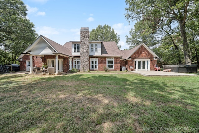 rear view of property with brick siding, a hot tub, a lawn, and french doors