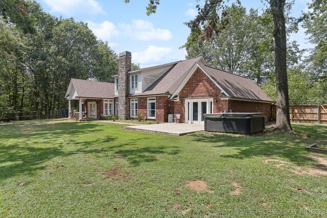 back of property featuring brick siding, fence, a yard, french doors, and a hot tub