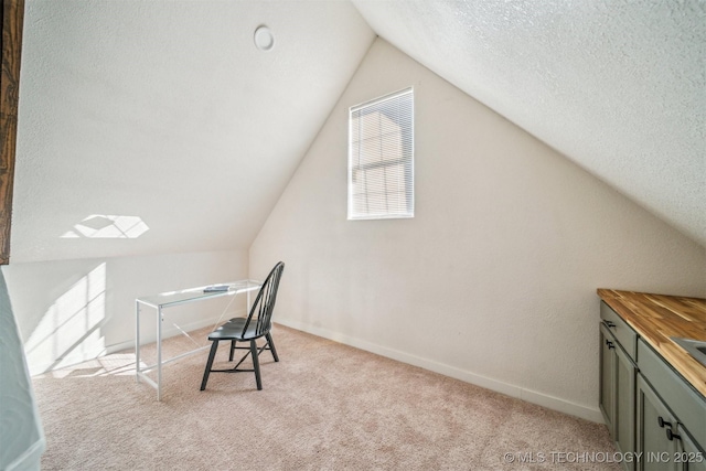 unfurnished office featuring carpet floors, vaulted ceiling, a textured ceiling, and baseboards