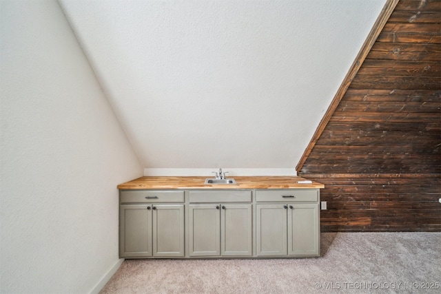 bathroom with wooden walls, vaulted ceiling, and a sink