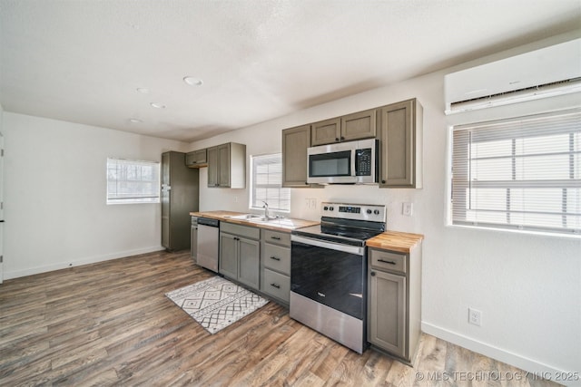 kitchen featuring stainless steel appliances, a sink, wood finished floors, butcher block countertops, and baseboards