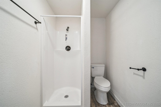 bathroom featuring wood finished floors, a shower stall, toilet, and baseboards