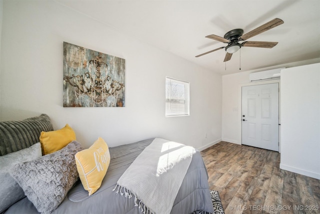 bedroom featuring a ceiling fan, an AC wall unit, baseboards, and wood finished floors