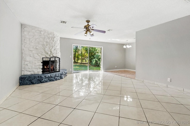 unfurnished living room featuring a textured ceiling, tile patterned flooring, ceiling fan with notable chandelier, a fireplace, and visible vents