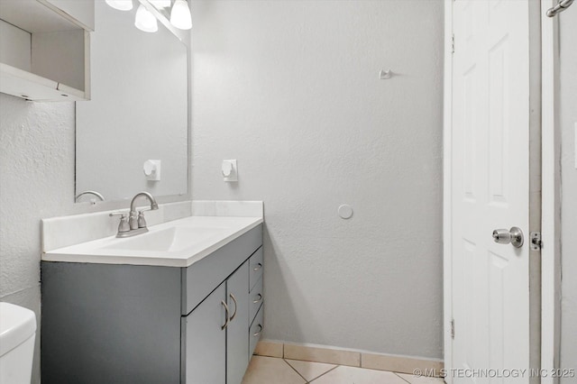 bathroom featuring a textured wall, toilet, vanity, tile patterned flooring, and baseboards