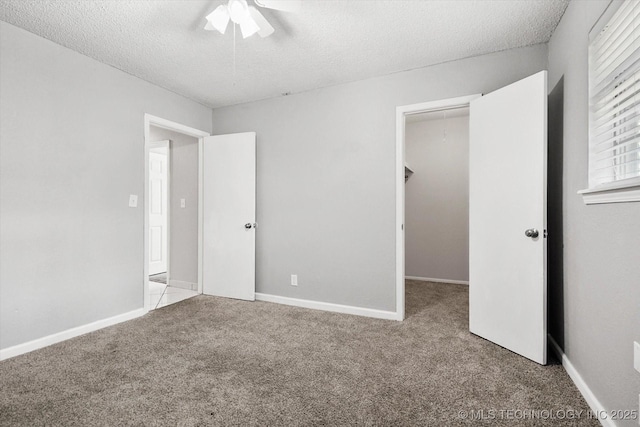 unfurnished bedroom with carpet floors, a walk in closet, ceiling fan, a textured ceiling, and baseboards