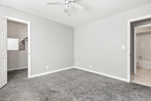 unfurnished bedroom with baseboards, tile patterned flooring, a spacious closet, a textured ceiling, and carpet flooring