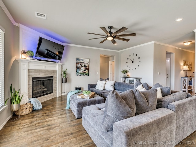 living area featuring a fireplace, wood finished floors, visible vents, a ceiling fan, and crown molding