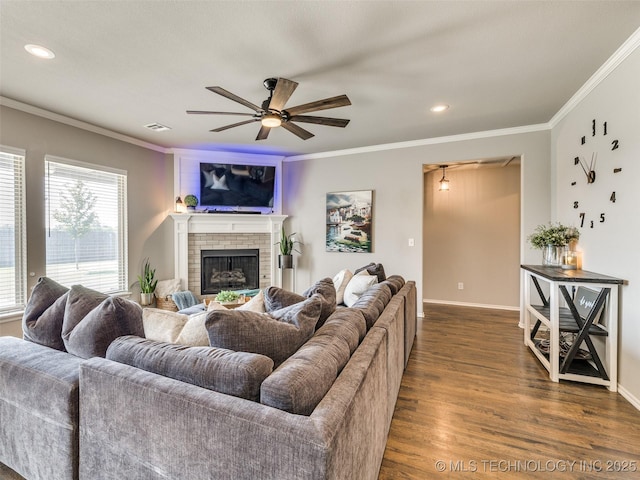 living room with ceiling fan, dark wood-style flooring, baseboards, a brick fireplace, and crown molding