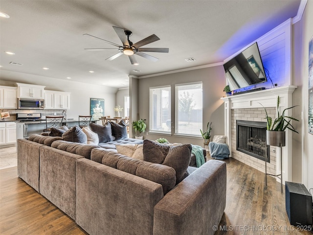 living area featuring visible vents, a fireplace, ornamental molding, and wood finished floors