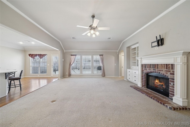 unfurnished living room featuring a brick fireplace, plenty of natural light, built in shelves, and crown molding