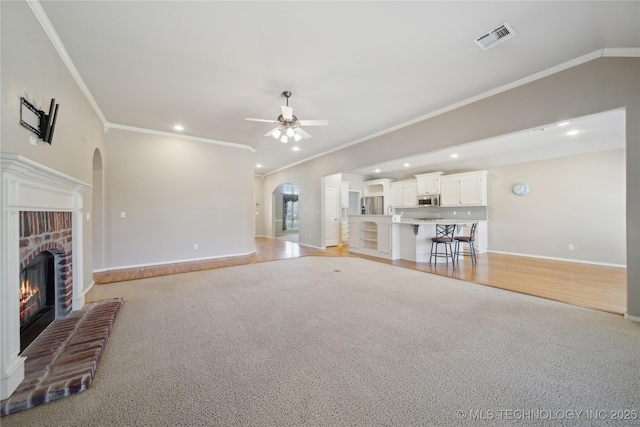 unfurnished living room with a ceiling fan, arched walkways, visible vents, and a fireplace