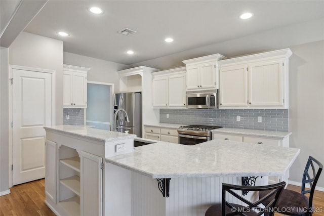 kitchen featuring wood finished floors, visible vents, white cabinets, appliances with stainless steel finishes, and an island with sink