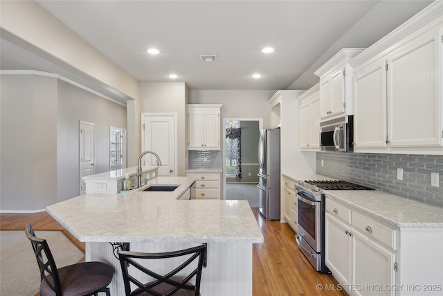 kitchen with a spacious island, visible vents, appliances with stainless steel finishes, white cabinets, and a sink