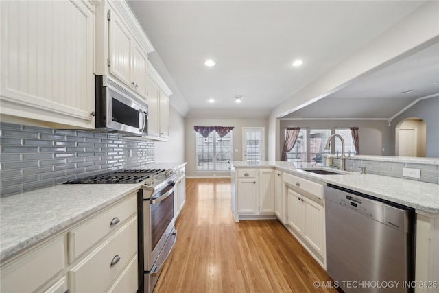 kitchen with stainless steel appliances, a sink, white cabinets, light wood-type flooring, and decorative backsplash