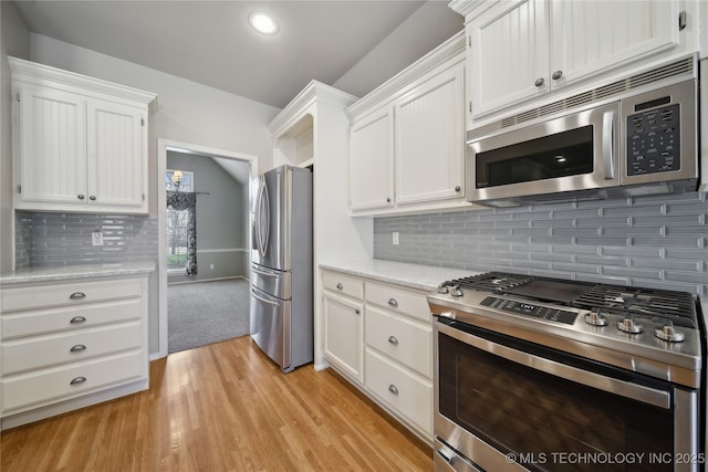 kitchen featuring tasteful backsplash, white cabinets, appliances with stainless steel finishes, light stone countertops, and light wood-style floors