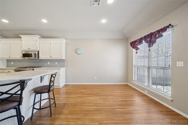 kitchen with tasteful backsplash, visible vents, stainless steel microwave, light countertops, and light wood-type flooring