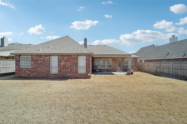 rear view of property featuring a patio area, a fenced backyard, a shingled roof, and brick siding