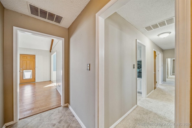 hall with a textured ceiling, light tile patterned floors, visible vents, and baseboards