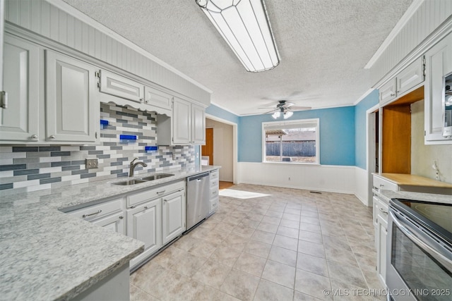 kitchen featuring a wainscoted wall, stainless steel appliances, ornamental molding, a sink, and ceiling fan