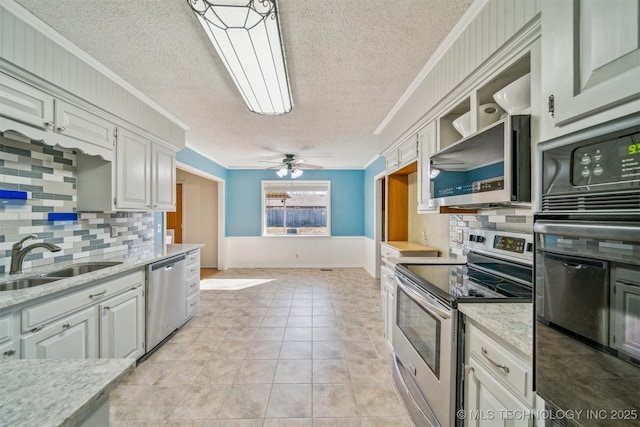 kitchen featuring light tile patterned floors, a wainscoted wall, ornamental molding, stainless steel appliances, and a sink