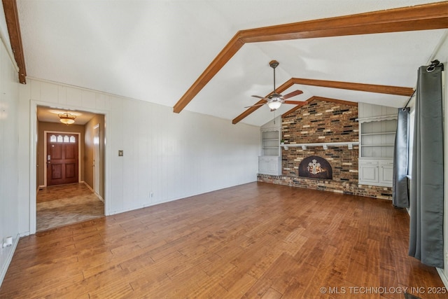 unfurnished living room featuring vaulted ceiling with beams, ceiling fan, built in shelves, a fireplace, and wood finished floors