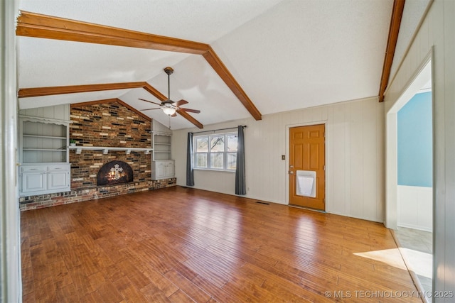 unfurnished living room featuring built in shelves, a fireplace, vaulted ceiling with beams, wood-type flooring, and a ceiling fan