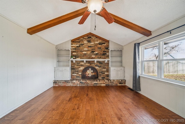 unfurnished living room featuring built in shelves, vaulted ceiling with beams, a fireplace, a textured ceiling, and hardwood / wood-style floors