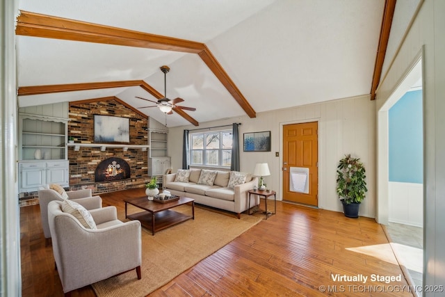 living room featuring built in features, vaulted ceiling with beams, a ceiling fan, a brick fireplace, and hardwood / wood-style flooring