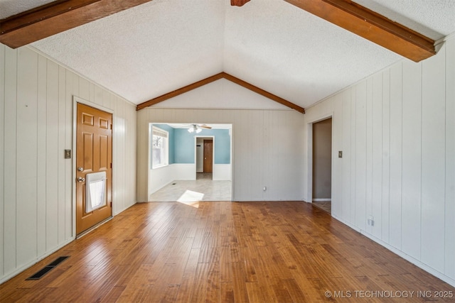 empty room with visible vents, a ceiling fan, hardwood / wood-style floors, vaulted ceiling with beams, and a textured ceiling