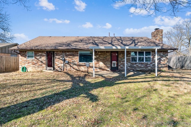 back of house featuring brick siding, fence, a chimney, and a lawn