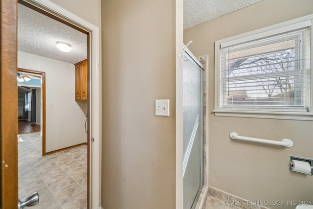 full bath with a shower stall, baseboards, and a textured ceiling