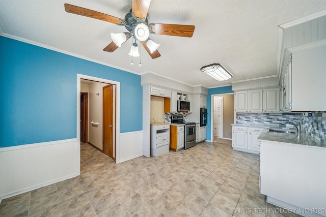 kitchen with decorative backsplash, wainscoting, appliances with stainless steel finishes, ornamental molding, and a sink