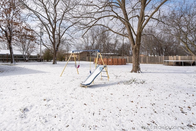 snowy yard with playground community, a trampoline, and fence