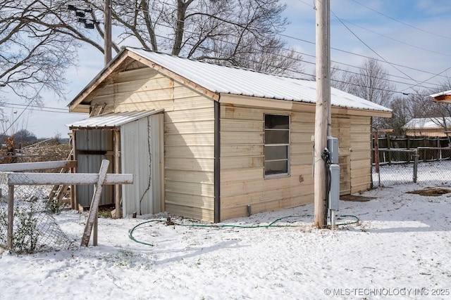 snow covered structure featuring an outdoor structure and fence