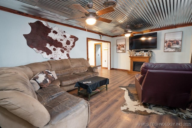 living area featuring a fireplace, crown molding, a ceiling fan, wood finished floors, and baseboards