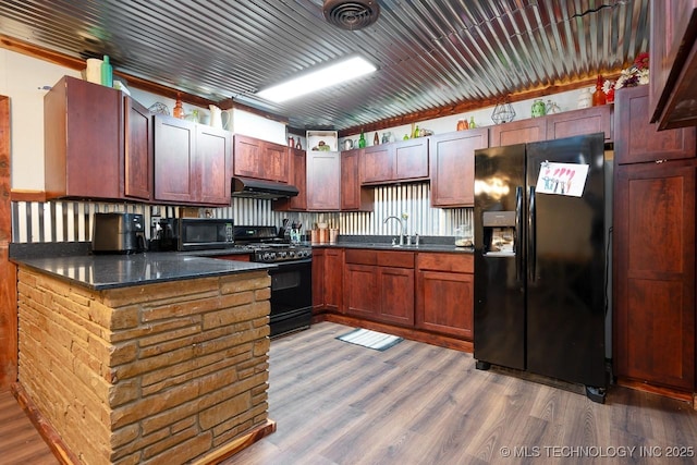 kitchen featuring under cabinet range hood, a sink, wood finished floors, visible vents, and black appliances