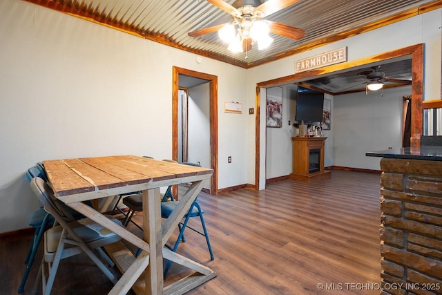 dining room featuring ceiling fan, a fireplace, wood finished floors, baseboards, and ornamental molding