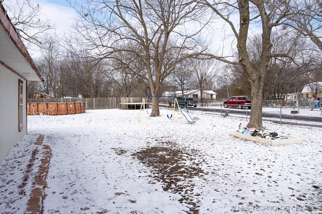 snowy yard with a trampoline, fence, and a playground