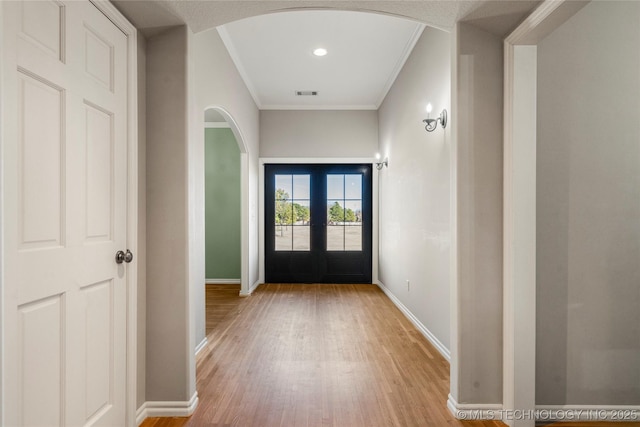 foyer with light wood finished floors, visible vents, arched walkways, baseboards, and french doors